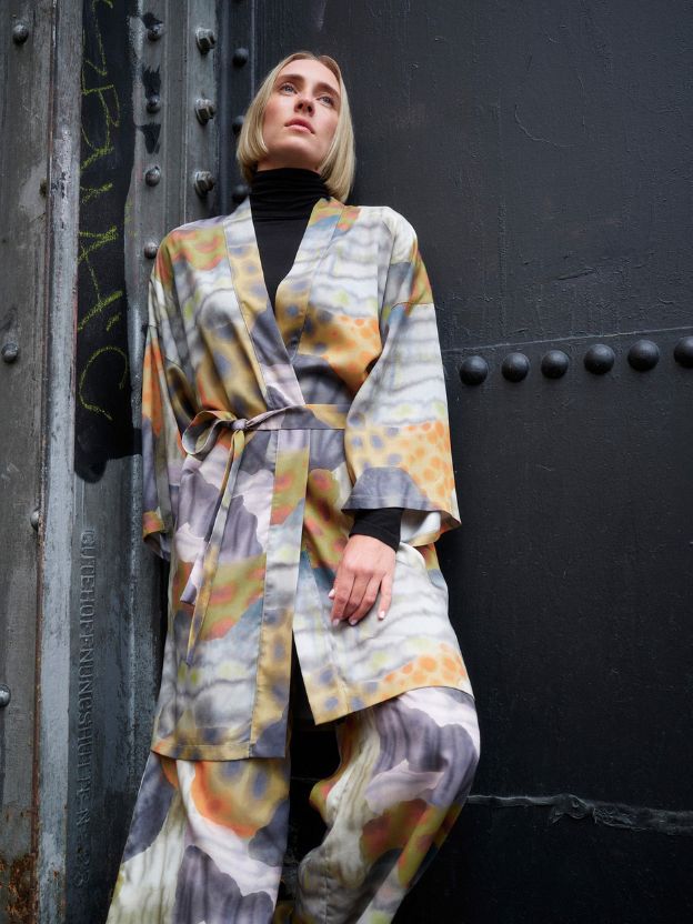 Two women laugh in a yard in front of a building in colorful summer dresses