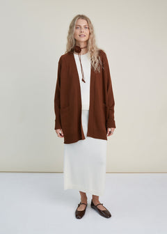 Woman wearing a brown cardigan over a white outfit on a plain background