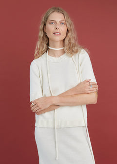 Woman wearing a white merino knit t-shirt against a red background