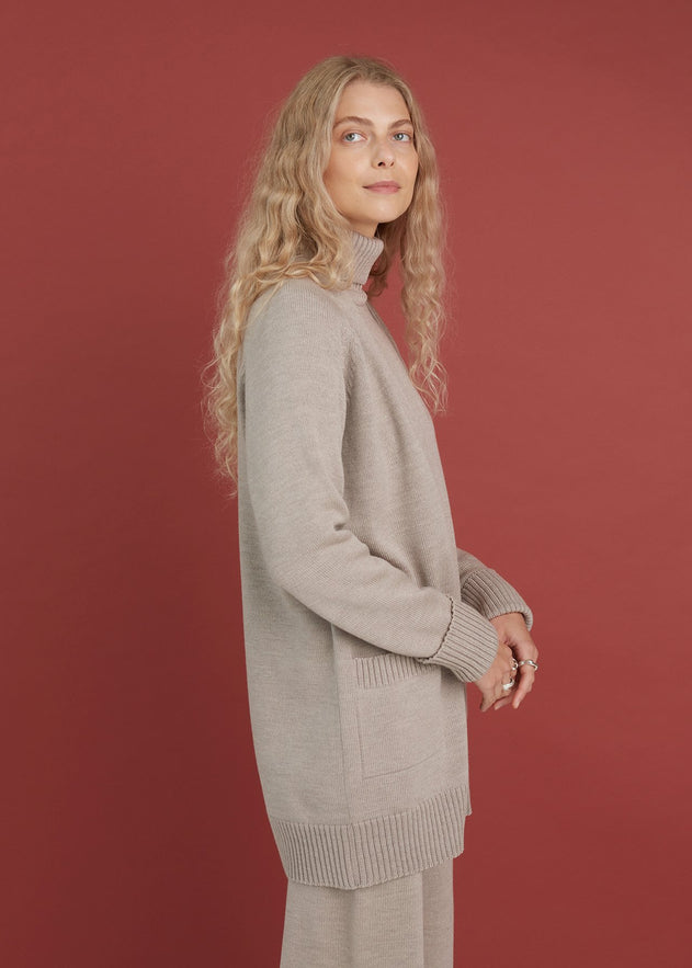 Woman wearing a long beige sweater against a red background