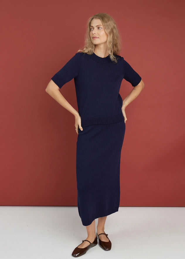 Woman wearing a navy merino blue dress against a red background