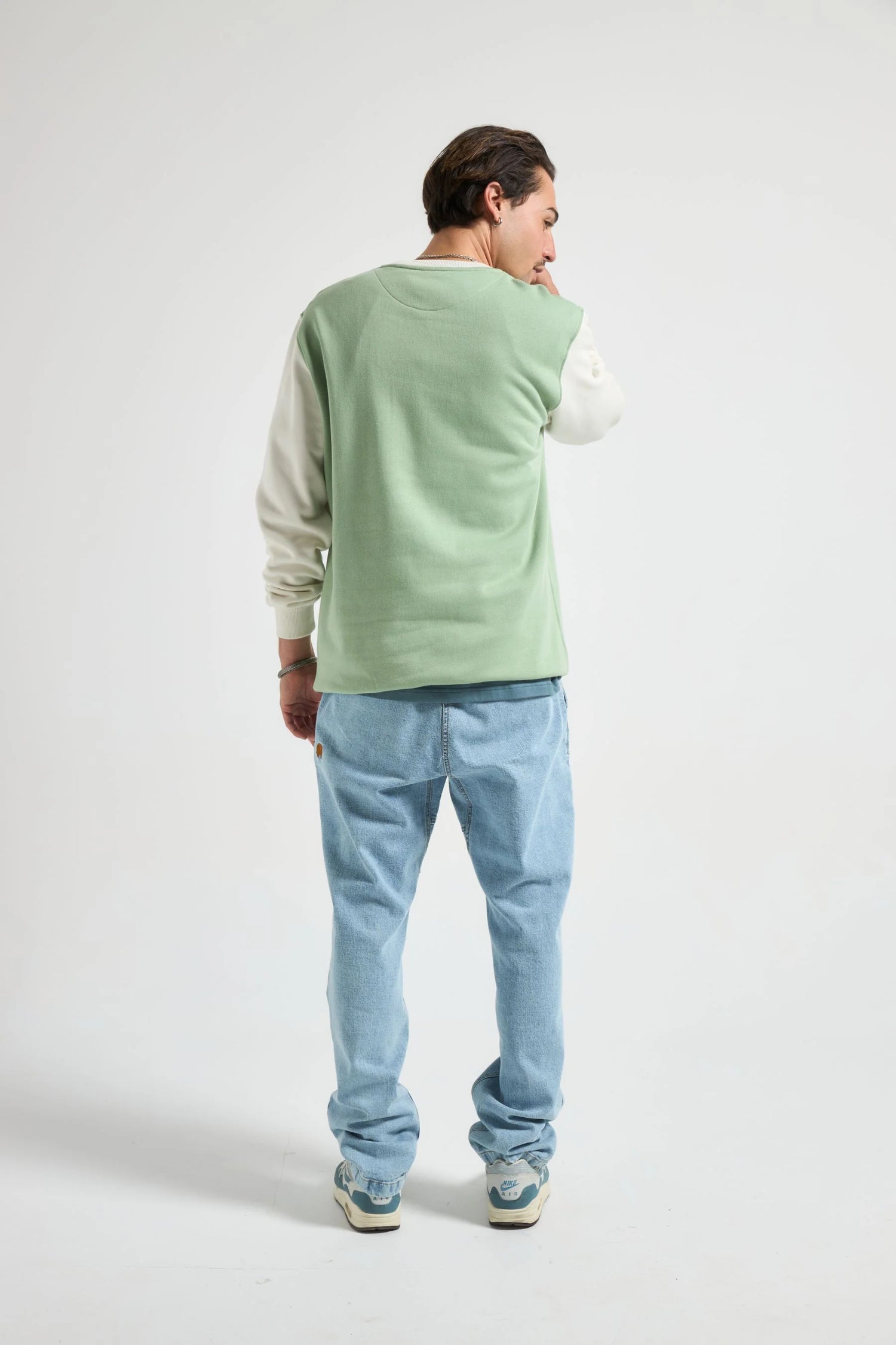 Person wearing a light green sweater over a white shirt with blue jeans on a white background