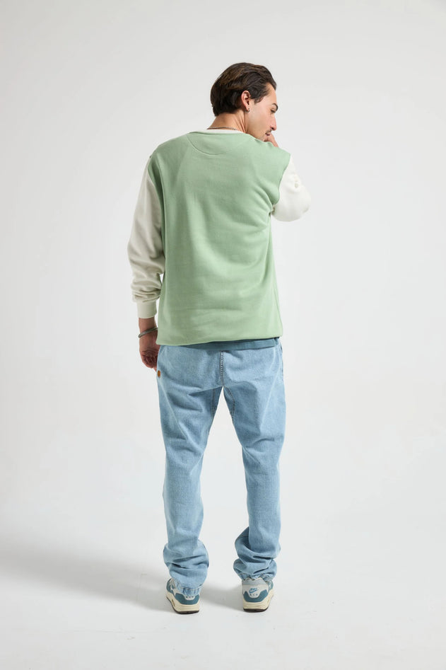 Person wearing a light green sweater over a white shirt with blue jeans on a white background