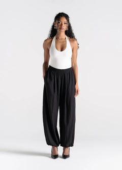 Woman wearing a white halter top and black wide-leg pants on a white background