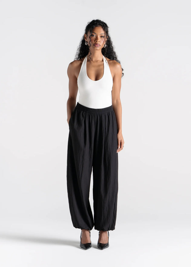 Woman wearing a white halter top and black wide-leg pants on a white background