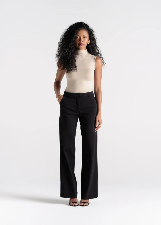 Woman wearing a beige top and black pants on a white background
