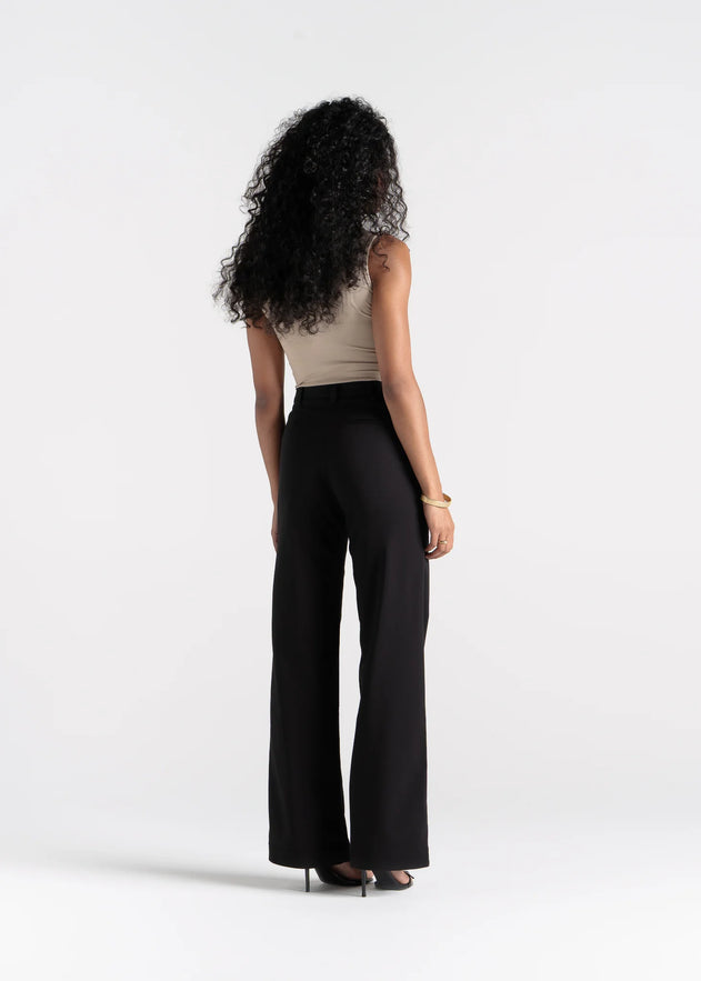 Woman wearing a beige top and black high-waisted pants on a white background