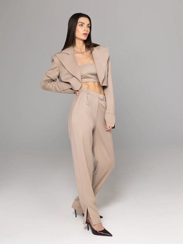 Woman wearing a beige suit with a cropped blazer and high-waisted pants on a gray background