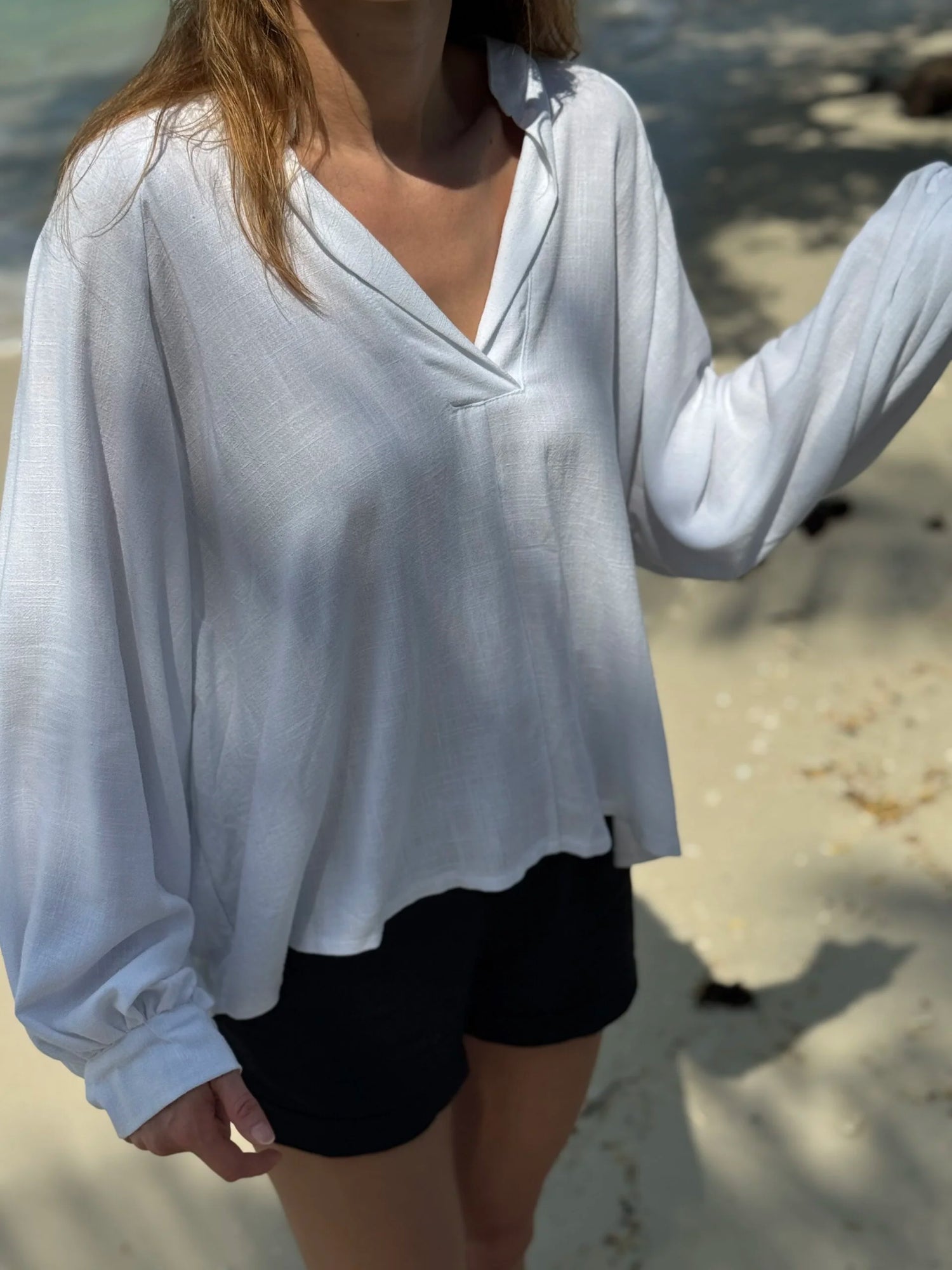 Person wearing a white long-sleeve top and black shorts on a beach.