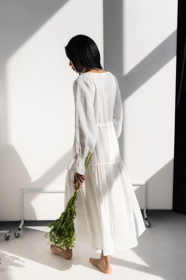 Person wearing a white dress holding greenery in a minimalistic setting