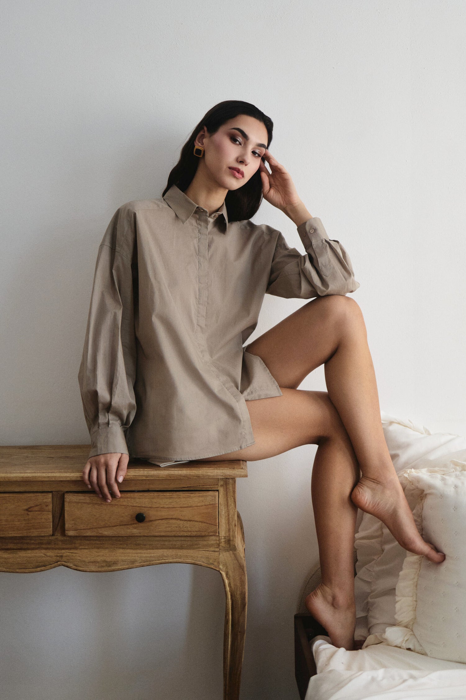 Woman in a beige shirt sitting on a wooden table against a white wall.