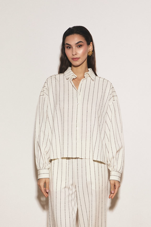 Woman wearing a white and beige striped outfit against a plain background