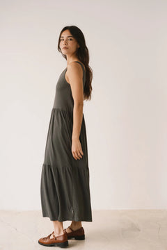 Woman wearing a dark green tiered dress against a plain background