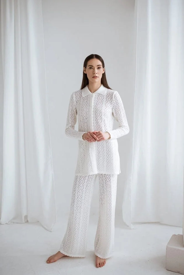 Woman wearing a white lace outfit standing against a white curtain.