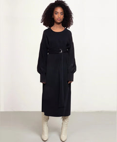 Woman wearing a black dress with a belt and white boots on a white background