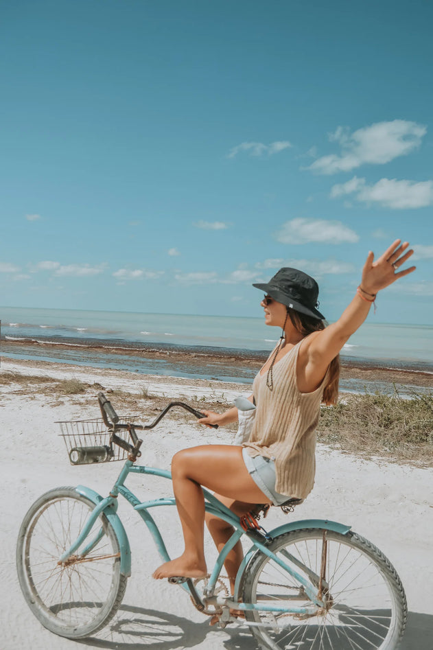Woman riding a bicycle on a beach with a clear blue sky.