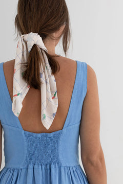 Woman wearing a blue dress with a white scarf tied around her hair on a plain background