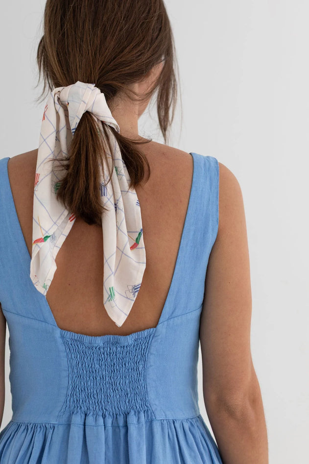 Woman wearing a blue dress with a white scarf tied around her hair on a plain background