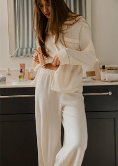 Woman in a cream ribbed lounge set standing in a bathroom.