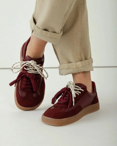 Maroon sneakers with white laces worn by a person in beige pants on a light background