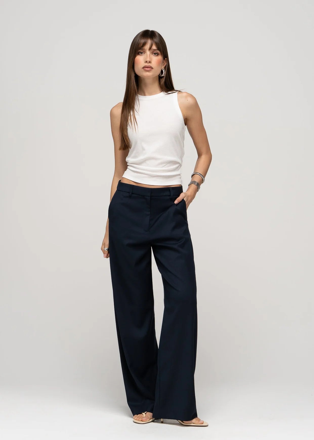 Woman wearing a white sleeveless top and navy wide-leg pants on a light gray background