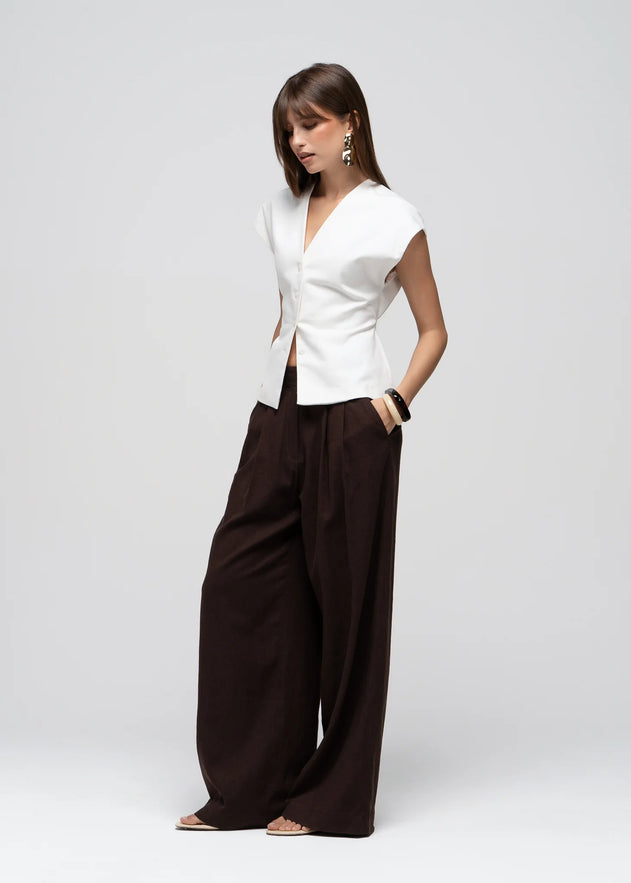 Woman wearing a white top and brown wide-leg pants on a light gray background