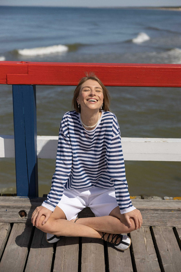 Woman sitting on a wooden pier by the water, smiling.
