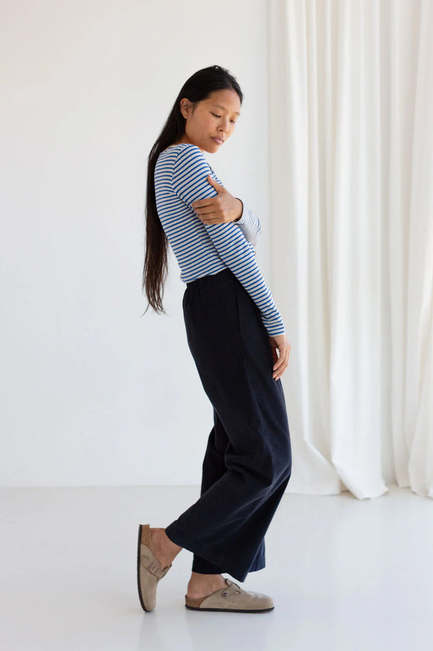 Woman wearing a striped shirt and dark pants standing against a white curtain.