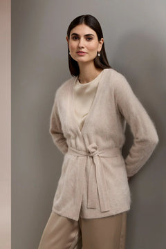 Woman wearing a beige belted cardigan and pants against a gray background