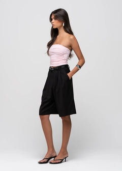 A woman modeling a light pink strapless ruched tube top and black high-waisted culotte shorts with a matching black belt, paired with black heeled sandals, against a light gray studio background.