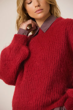 A close-up of a woman wearing a chunky, fuzzy red knit sweater layered over a collared shirt with a burgundy and beige stripe pattern.