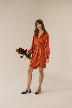 Woman wearing a rust-colored dress holding flowers against a beige background
