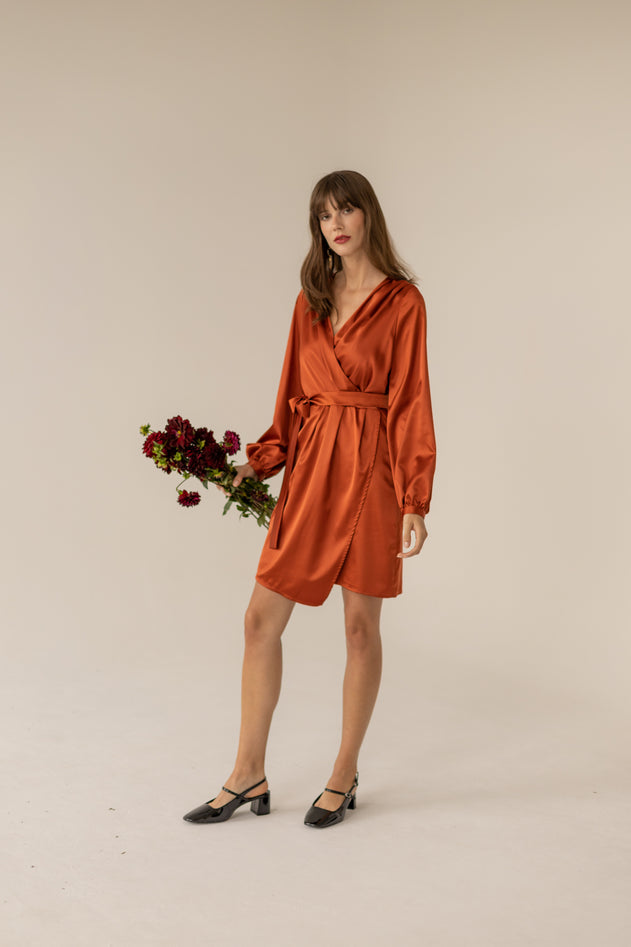 Woman wearing a rust-colored dress holding flowers against a beige background