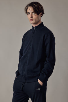 Man wearing a black quarter-zip sweatshirt and pants against a neutral background
