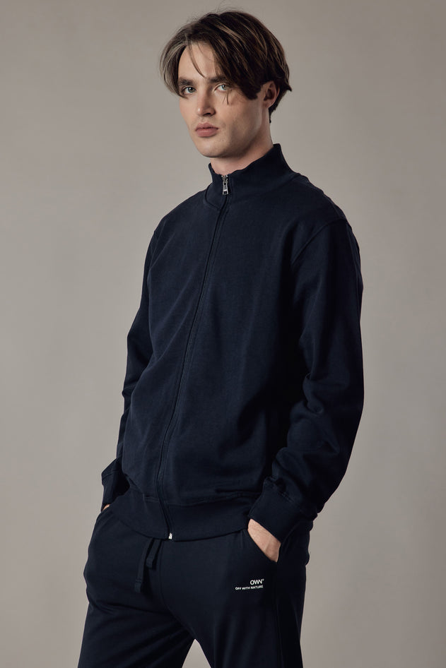 Man wearing a black quarter-zip sweatshirt and pants against a neutral background