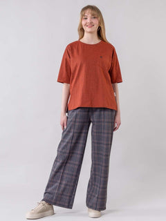 Person wearing a rust-colored t-shirt and plaid pants on a white background